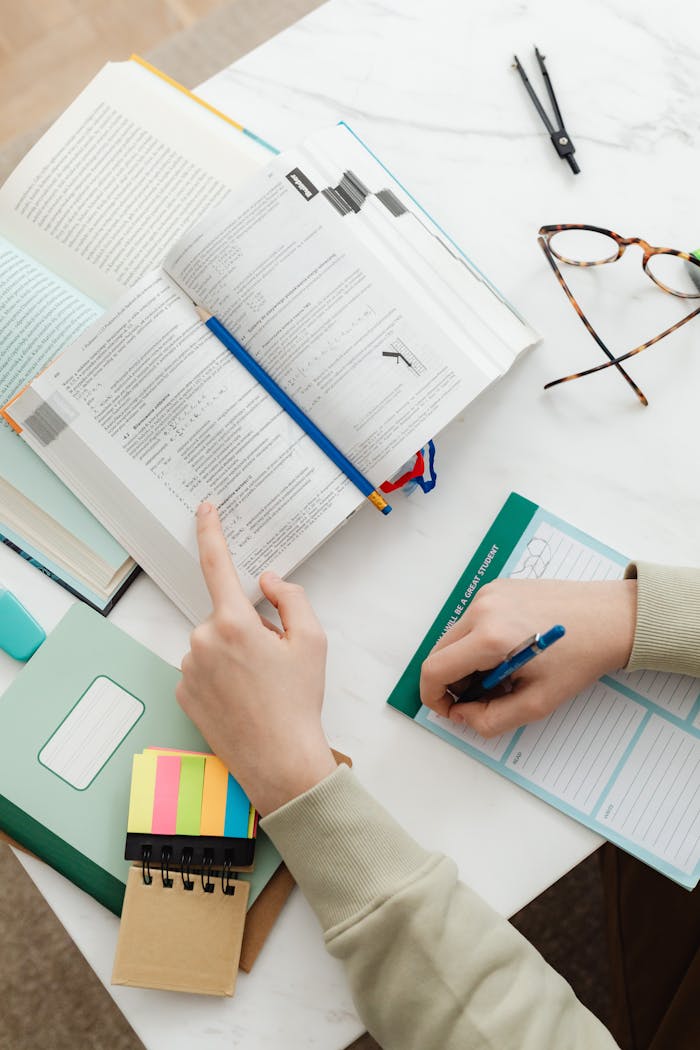 Close-up of a student studying with books and notes on a white desk.